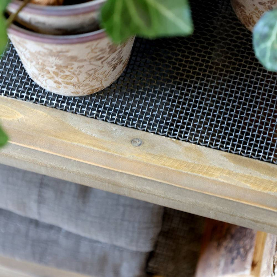 Masszív fémhálós polc fa keretbe foglalva, növényekkel és textíliával.