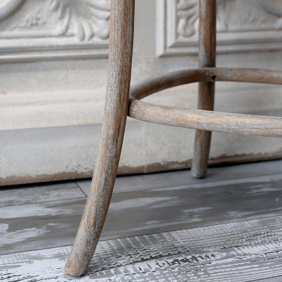 A bárszék lábrésze és hajlított lábtartója közelről, rusztikus padlón