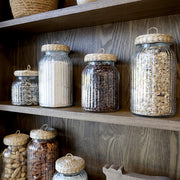 Üvegedények sorakoznak az Old French vitrines szekrény polcain, natúr fa hátlap előtt.