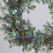 Koszorú részlet közelről kék bogyókkal és tobozzal.