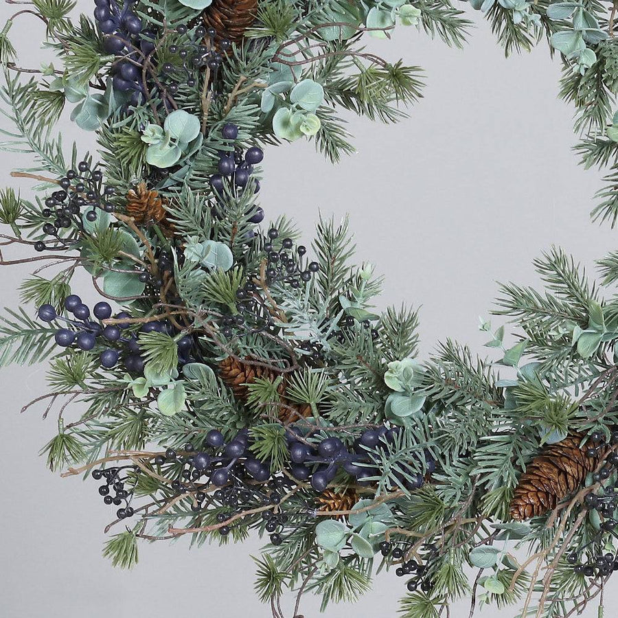 Koszorú részlet közelről kék bogyókkal és tobozzal.