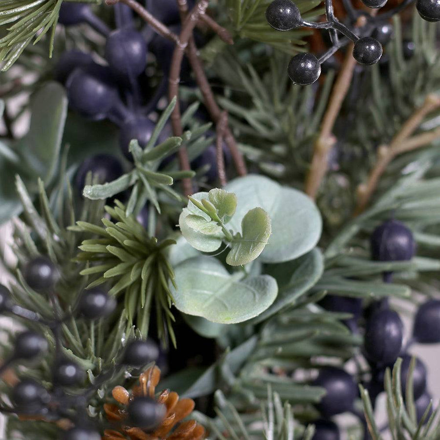 Koszorú közelről, zöld levelek és kék bogyók részletfotója.