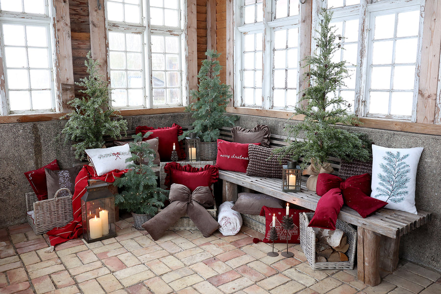 Havas hatású PINE műfenyő nagy ablak mellett, karácsonyi párnákkal díszített padnál