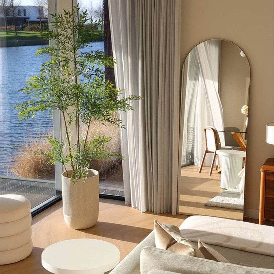 Élethű, levelekkel gazdagon borított mű ruszkusz növény modern kaspóban, nappali sarokban elhelyezve.