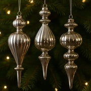 Ezüst üveg jégcsap díszek karácsonyfán, meleg fényekkel megvilágítva.