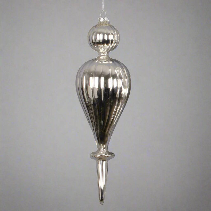 Egy ezüst, csepp formájú, bordázott üveg karácsonyfadísz közelről.