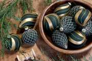 Olívazöld-arany Shiny üvegdíszek sötétzöld, rácsmintás díszekkel egy fatálban, örökzöld ágak között.