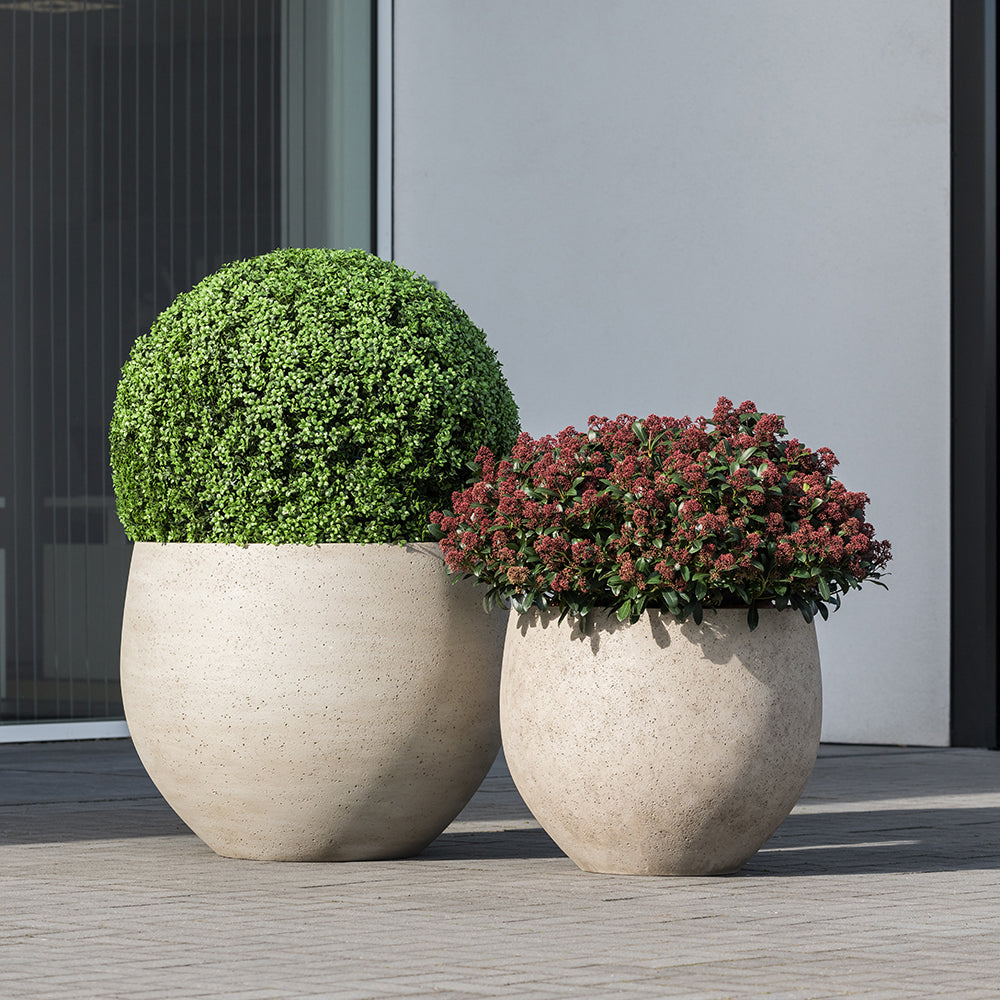 Betonhatású kaspók kültéren, modern épület előtt, zöld és piros növényekkel beültetve – Pottery Pots Urban kollekció