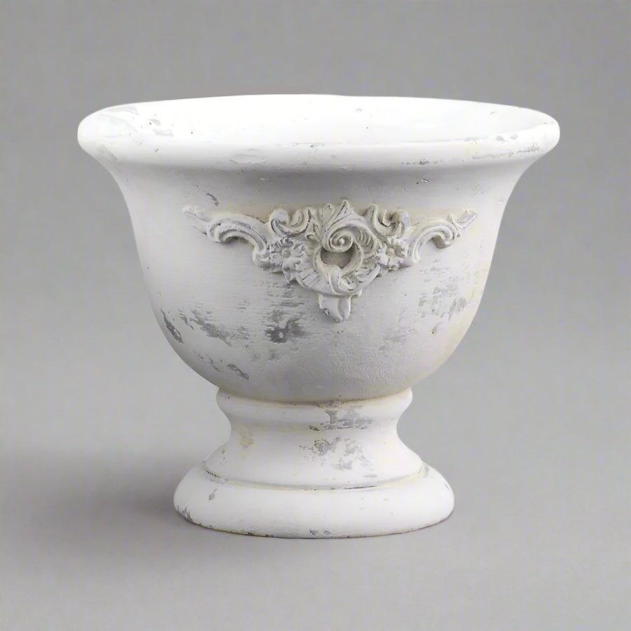 Rusztikus hatású, talpas cement kaspó kopottas, törtfehér felülettel, klasszikus formában.