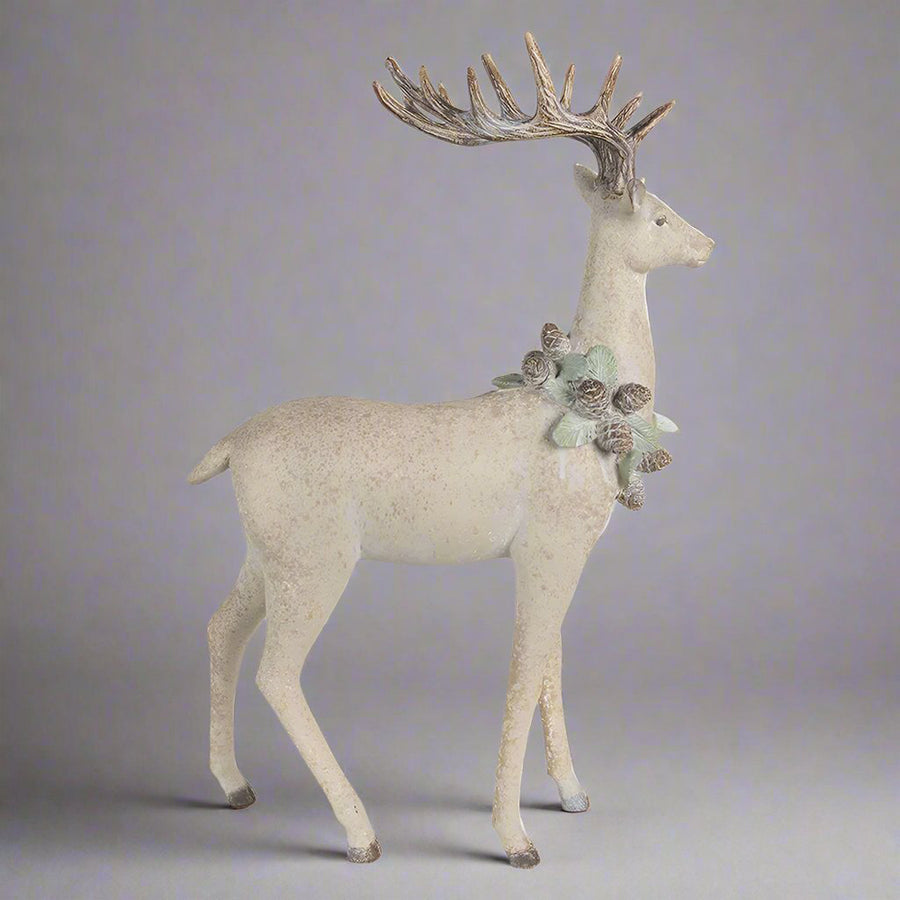Tobozkoszorúval díszített, bézs színű, karácsonyi szarvas figura.