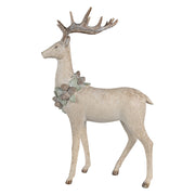 Tobozkoszorúval díszített, bézs színű, karácsonyi szarvas figura.