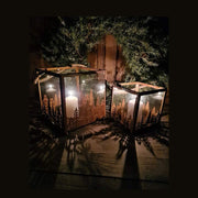 Vidéki rusztikus stílusú, antikolt rozsdás színű 2 darabos karácsonyi sziluettes fém lámpásszett fenyőkoszorú előtt antik faasztalon