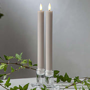 Bézs LED vacsoragyertyák dekor pohárban, meleg fényű lánggal, természetes zöld díszítéssel és elegáns hangulatban elrendezve.