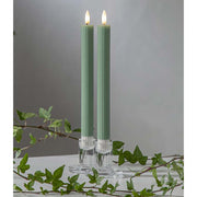 Zöld LED vacsoragyertyák dekor pohárban, meleg fényű lánggal, természetes zöld díszítéssel és elegáns hangulatban elrendezve.