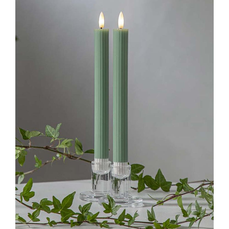 Zöld LED vacsoragyertyák dekor pohárban, meleg fényű lánggal, természetes zöld díszítéssel és elegáns hangulatban elrendezve.