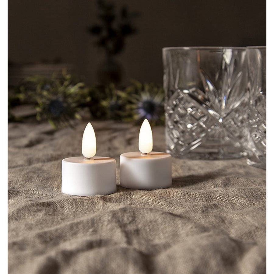 2 darabos LED gyertya, üvegpoharakkal asztalon. 