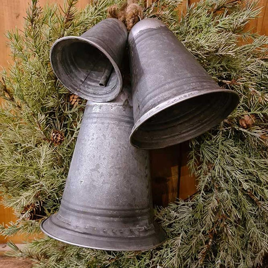 Rusztikus vidéki stílusú, óriás méretű, 14-21-29 cm magas, antikolt felületű, 3 darabos karácsonyi kézműves bádogharang szett fenyőkoszorún 