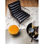 Modern nappaliban álló fekete műbőr fotel, sárga bársony puffal és asztallal.