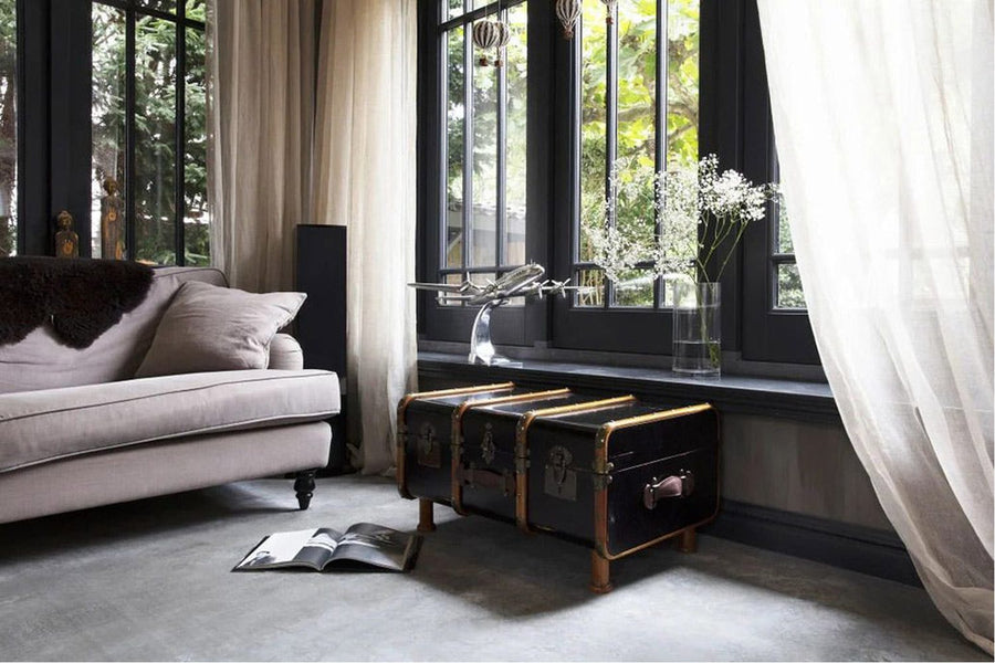 Kortárs nappaliban, ablak előtt álló utazóláda formájú dohányzóasztal.