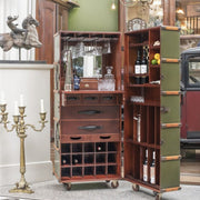 Vintage stílusú nappaliban álló zöld és mahagóni színű, görgős utazóláda-bárszekrény