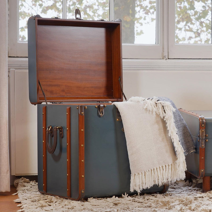 Hálószobában álló nyitott fedelű utazóláda kisasztal, takaróval.