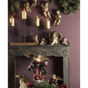 Barokk stílusú, 34 cm magas, falra függeszthető harsonás angyal figura lila színű karácsonyi falon kandallóval és gyertyatartóval 