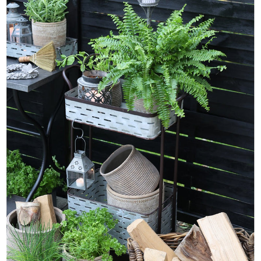 Hangulatkép: a görgős virágállvány egy teraszon, rajta növények, kaspók, lámpások.