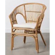 Fedett teraszon álló natúr színű, rattanból készült kézműves karosszék törtfehér ülőpárnával.