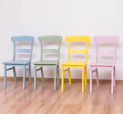 Beltérben egymás mellett álló kék, zöld, sárga és rózsaszín fenyőfa étkezőszékek.