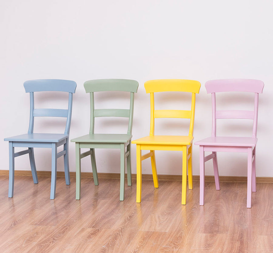 Beltérben egymás mellett álló kék, zöld, sárga és rózsaszín fenyőfa étkezőszékek.