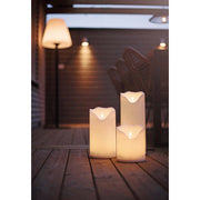 Kültéri terasz padlóján álló, három különböző méretű fehér színű LED gyertya.