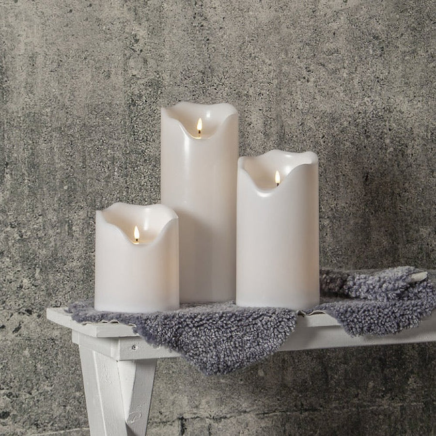 Élethű, meleg fehér fényű, fehér színű LED gyertyák kültéri padon.