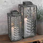 Kültéri konzolasztalon álló vintage, fém lámpások, dekoratív levélmotívummal díszítve.