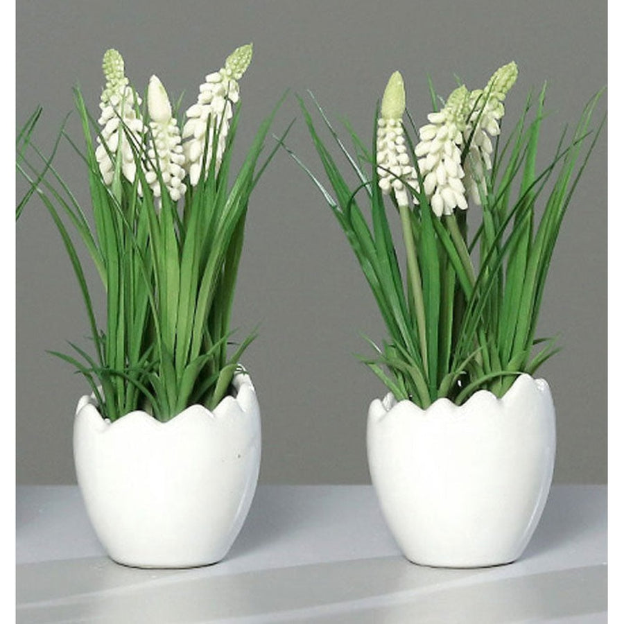 Krém színárnyalatú mű gyöngyike virág, tojás formájú, fehér színű kerámia kaspóban.