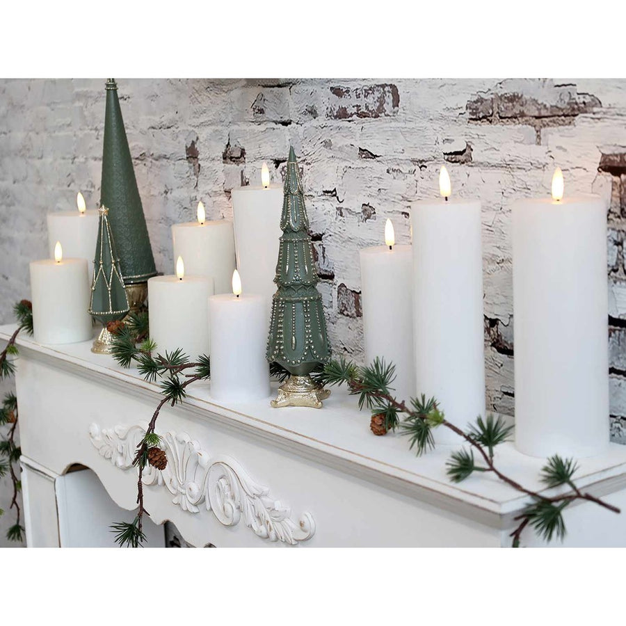 Mű ciprus girland, fehér kandallópárkányon, zöld dekor fenyőfákkal és fehér gyertyákkal.