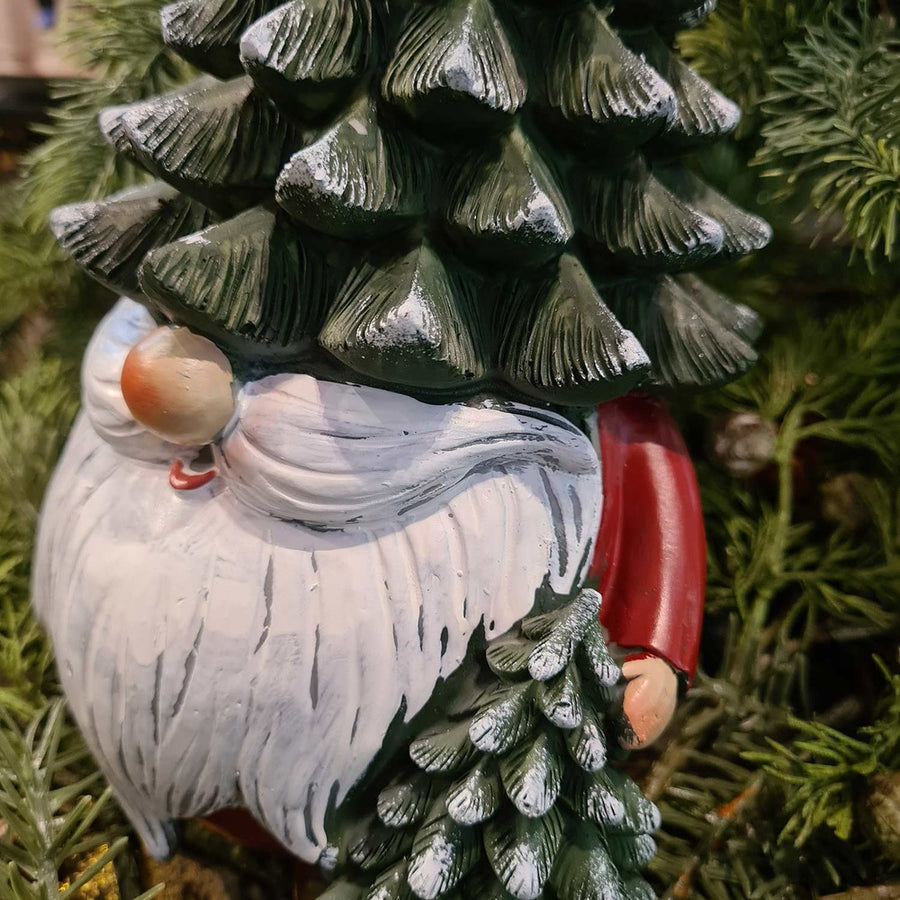 Karácsonyi manó fenyősapkában, zöld fenyők között.