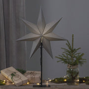 Szürke színű világító karácsonyi papírcsillag, ajándékokkal és fenyőággal.