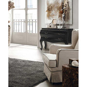 Fekete színű mahagónifa komód bézs fotellel, világos szobában. 