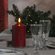 Prémium minőségű, élethű megjelenésű, meleg fehér fényű realisztikus LED lánggal és bordó színű valódi viasztestből kialakított, időzítővel rendelkező 15 cm magas LED oszlopgyertya  ünnepi karácsonyi asztalon üvegpoharakkal 
