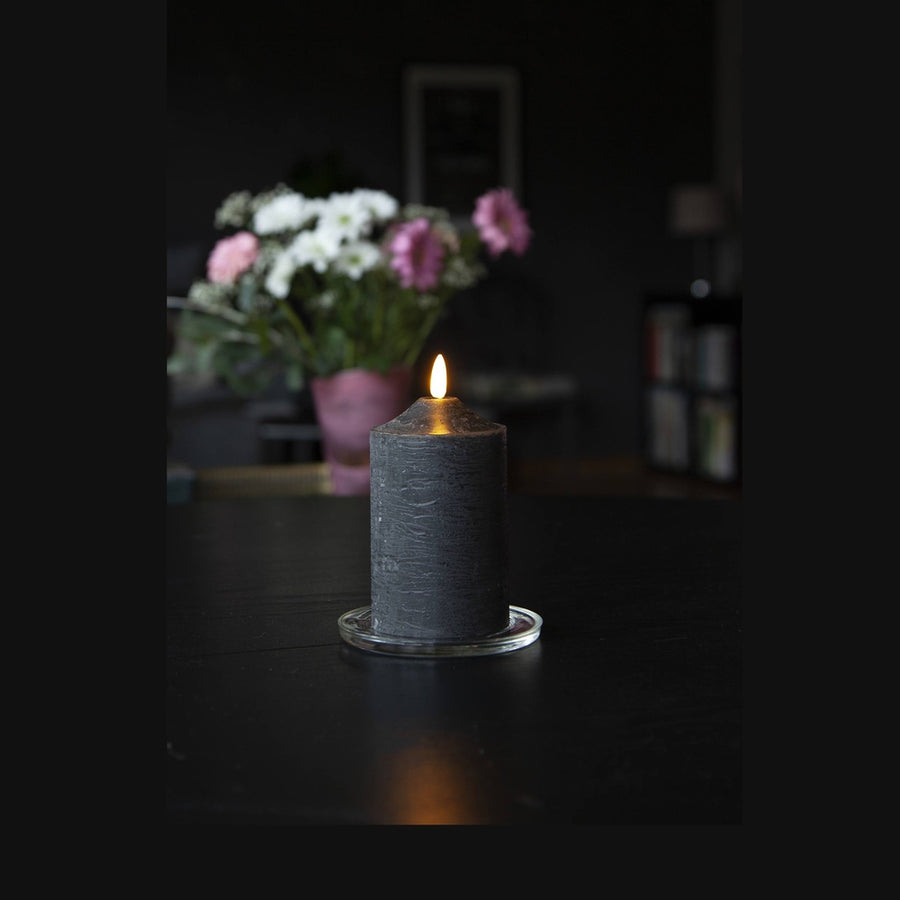 Fekete színű LED gyertya asztalon, virágcsokorral.