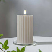 Bézs Stripe LED gyertya dekor pohárban elhelyezve, meleg fényben világítva, zöld növényi elemekkel körülvéve, meghitt beltéri hangulatban.