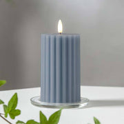 Kék Stripe LED gyertya dekor pohárban elhelyezve, meleg fényben világítva, zöld növényi elemekkel körülvéve, meghitt beltéri hangulatban.