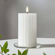Fehér Stripe LED gyertya dekor pohárban elhelyezve, meleg fényben világítva, zöld növényi elemekkel körülvéve, meghitt beltéri hangulatban.