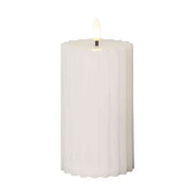 Fehér, valódi viaszból készült LED gyertya 15 cm magas, kannelúrás oszlopdizájnnal és meleg fényű pislákoló lánggal, elegáns dekorációhoz.