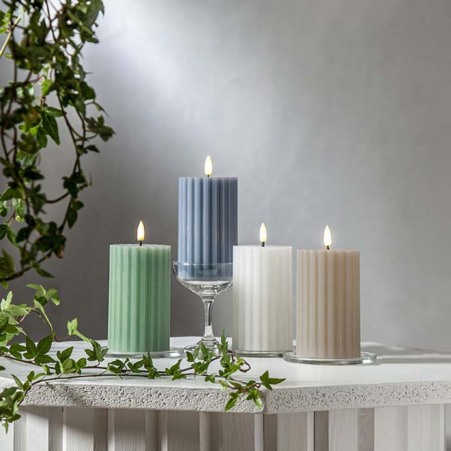 Stripe LED gyertyák különböző méretekben, fehér színben, kannelúrás oszlop formában, meleg fényű lánggal csoportosan elrendezve.