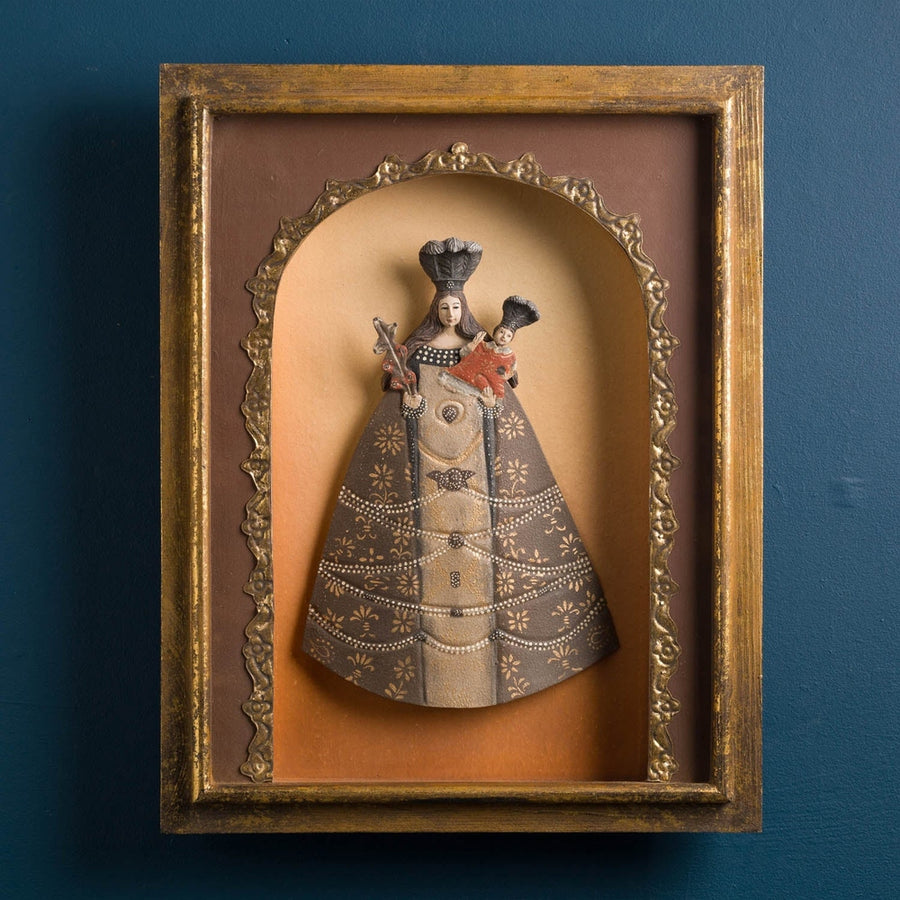 Szoborfülkés fa képkeretbe foglalt, a Liliomos Madonnát ábrázoló figura.