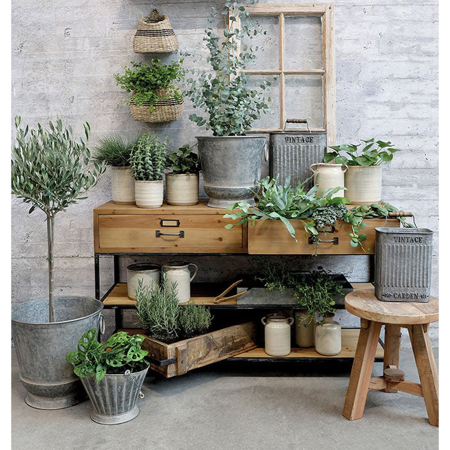 Natúr színű, loft stílusú 2 fiókos, 2 polcos konzolasztal, zöld növényekkel és kaspókkal.