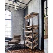 Loft stílusú bortartó polcos állvány, szürke fal előtt, megrakva borospalackokkal és poharakkal.