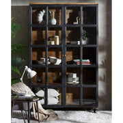 Loft stílusú, mangófából készült, 194 cm magas, 4 polcos, fémkerekekkel felszerelt vitrines szekrény fehér szőnyegen egy nappaliban, benne fehér étkészlettel 