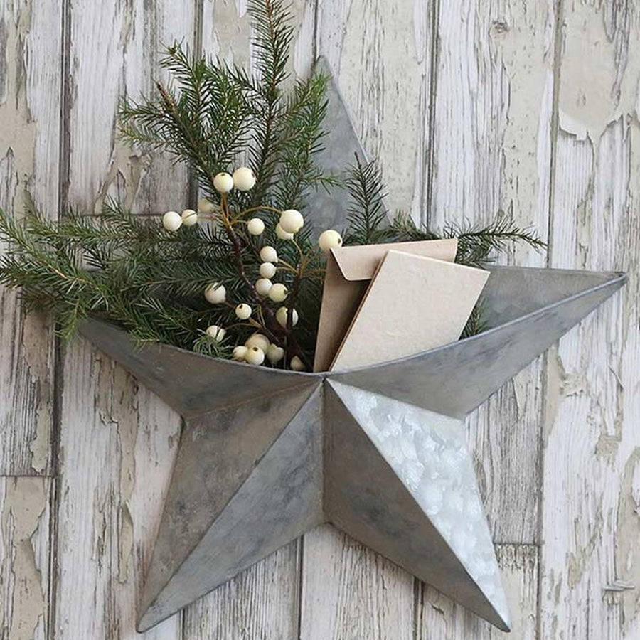 Karácsonyi bádog csillag, rusztikus fehér deszka falon, benne fenyőágak és bogyók. 